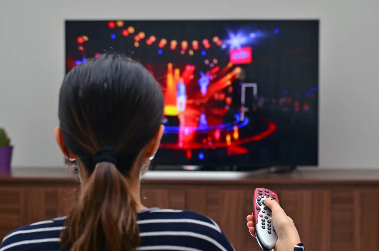 shutterstock_793438051-2 | TVGURU.cz Žena sedí u televize a míří na ni ovladačem.