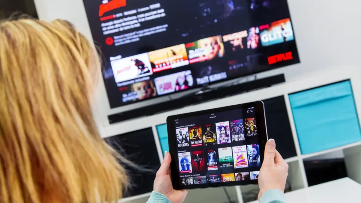 Žena má Netflix spuštěný na televizi i tabletu.