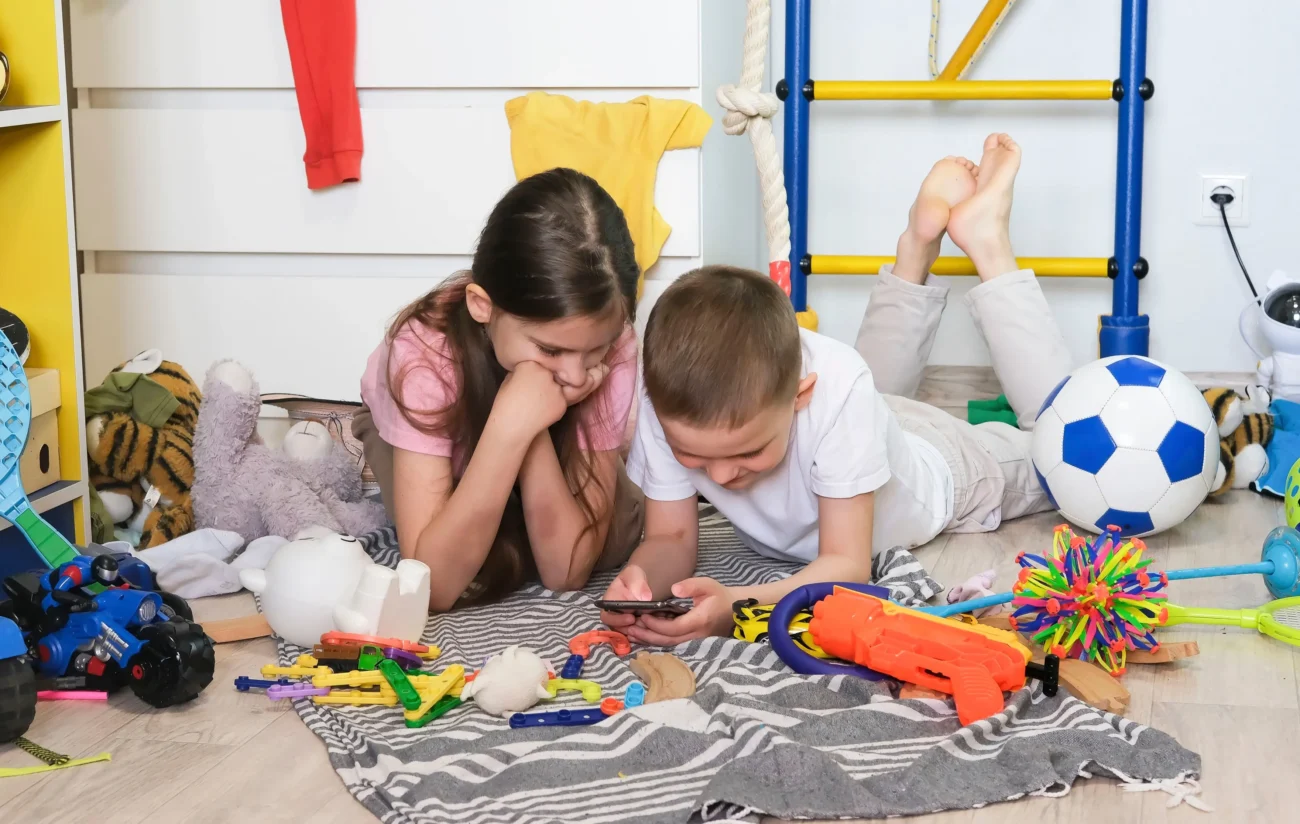 shutterstock_2468050207-2 | TVGURU.cz Děti leží v pokoji na zemi a jsou na mobilu.