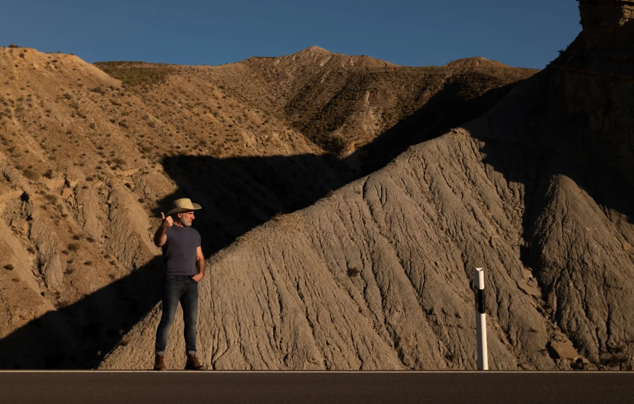 shutterstock_2116997177-2-2 | TVGURU.cz Muž stojí u silnice a stopuje.