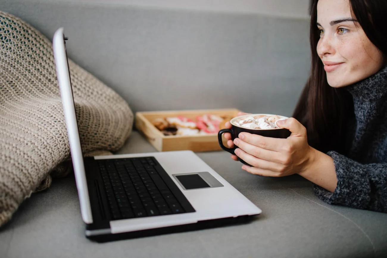 shutterstock_1797014188-2 | TVGURU.cz Žena leží u notebooku s hrnkem v ruce.