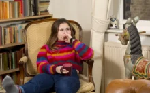 Slečna sedí ve svetru na křesle a kolem ní jsou knížky.