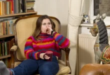 Slečna sedí ve svetru na křesle a kolem ní jsou knížky.