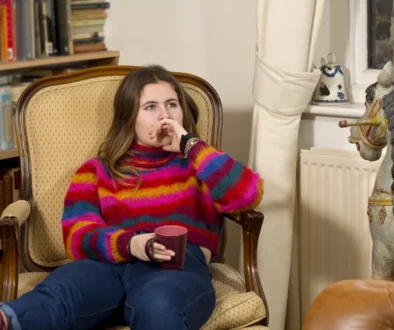 Slečna sedí ve svetru na křesle a kolem ní jsou knížky.