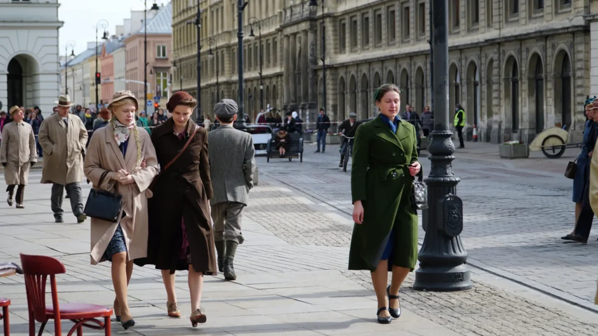 Dobově oblečené ženy se procházejí ulicemi.