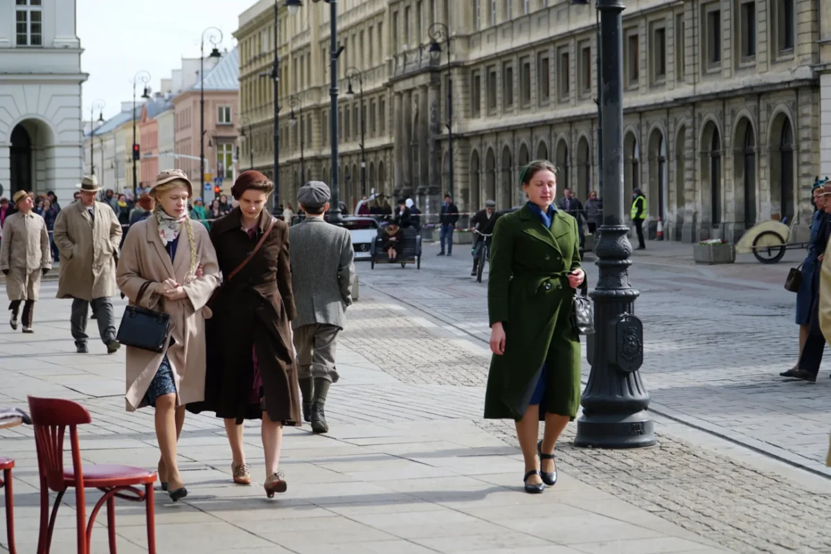 Dobově oblečené ženy se procházejí ulicemi.
