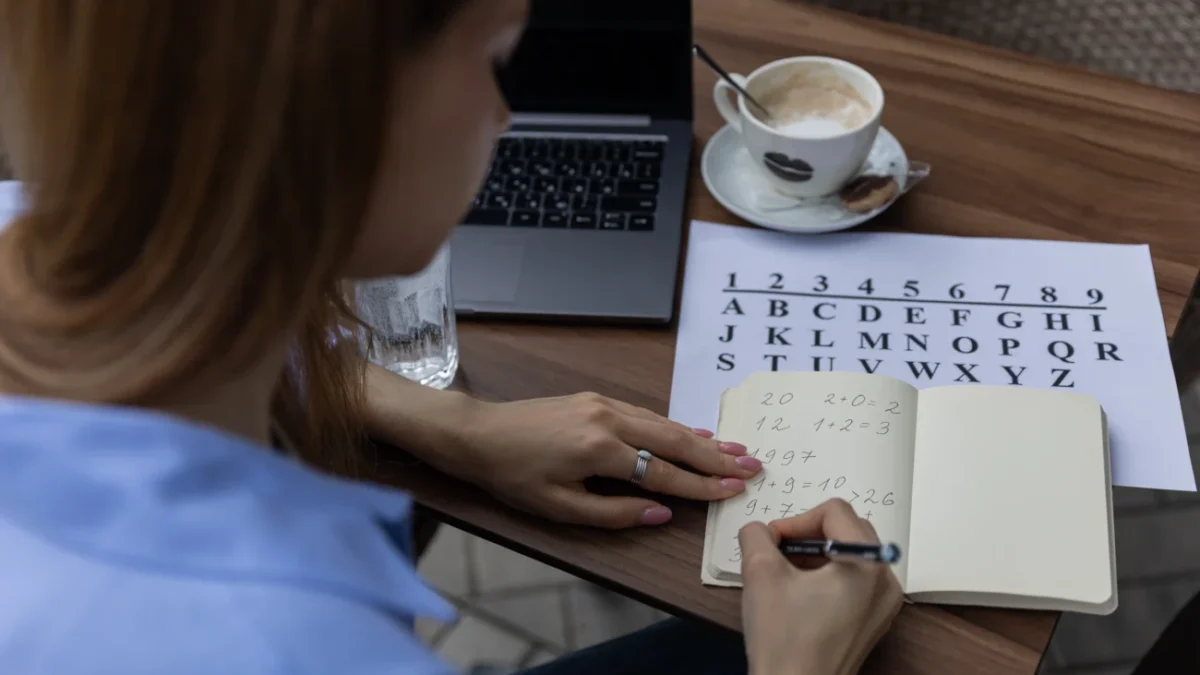 Žena sedí u stolu a píše si čísla do notesu.