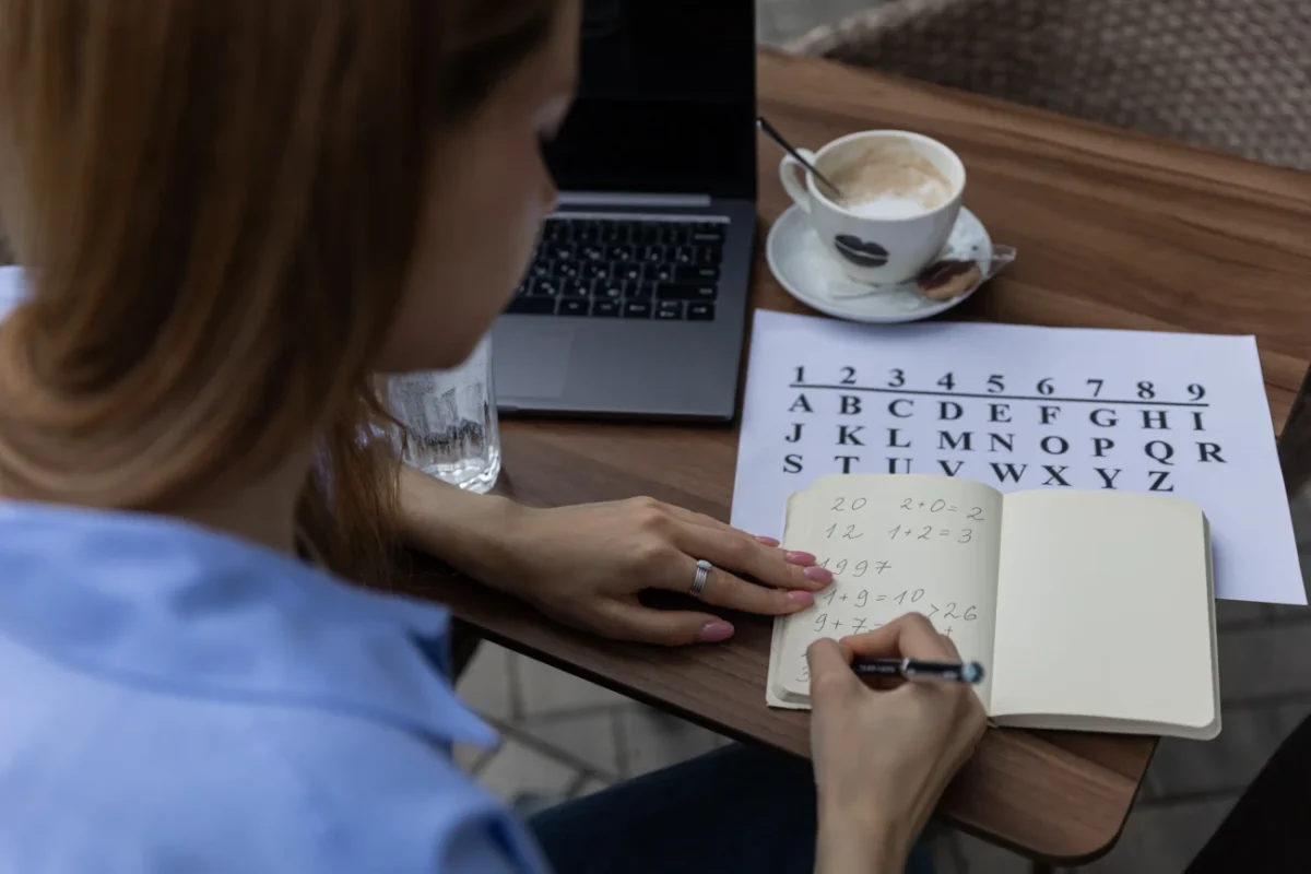 Žena sedí u stolu a píše si čísla do notesu.