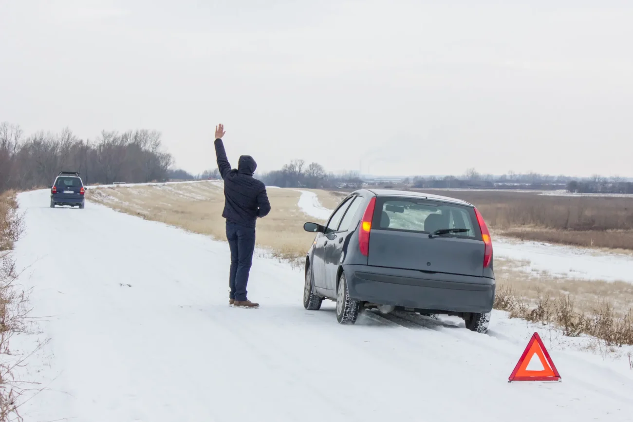 Muž stojící u auta na zasněžené silnici. 