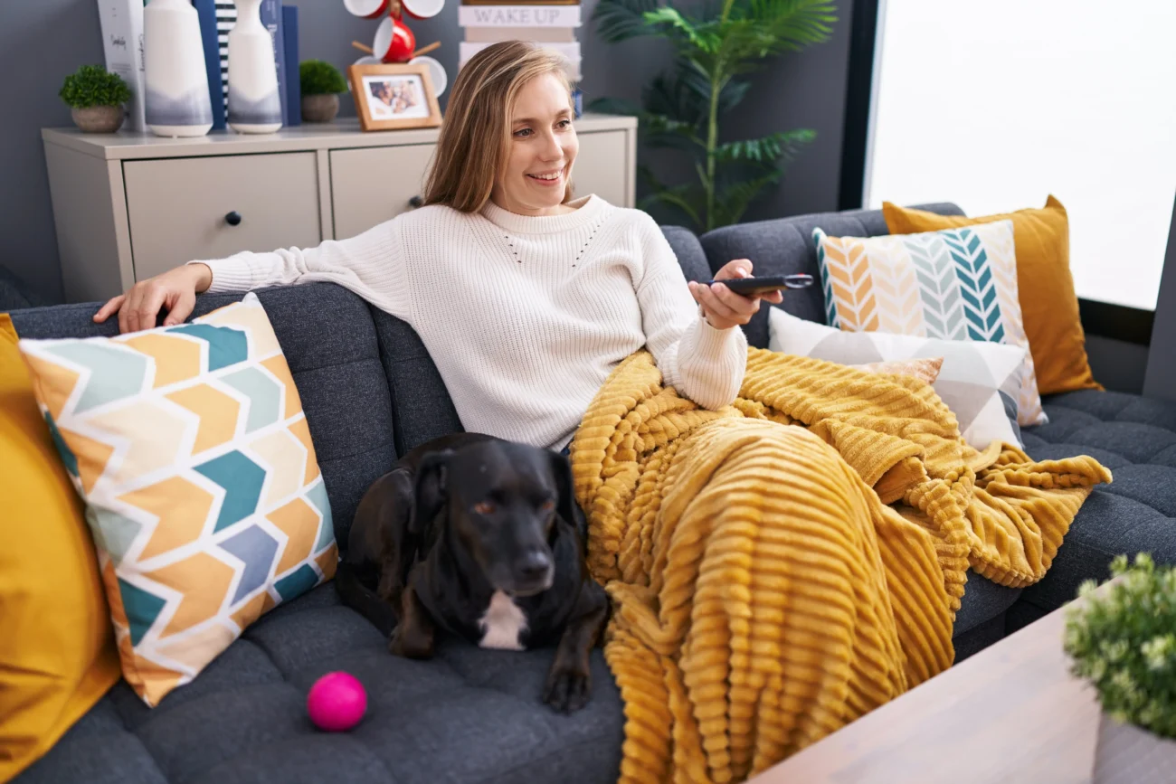 shutterstock_2399465331 1 | TVGURU.cz Žena sedí na gauči se psem a tv ovladačem v ruce.