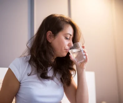 Žena sedí na posteli a popíjí vodu.