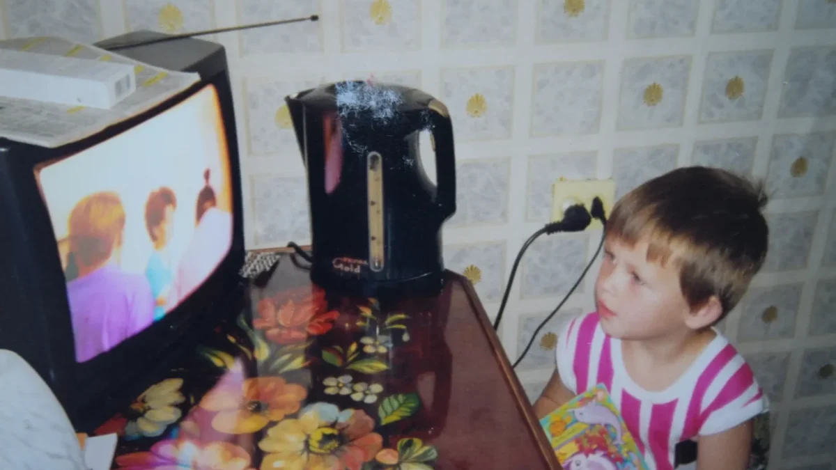 Dítě stojí v kuchyni a dívá se na TV.