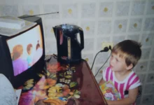 Dítě stojí v kuchyni a dívá se na TV.