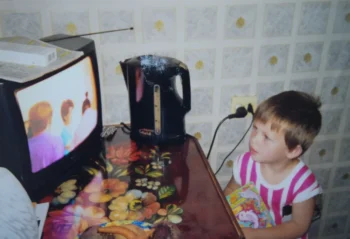 Dítě stojí v kuchyni a dívá se na TV.