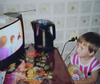 Dítě stojí v kuchyni a dívá se na TV.