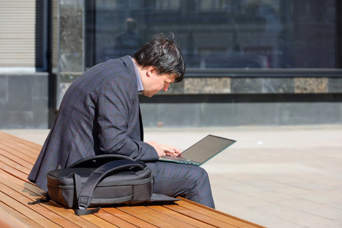 shutterstock_2607375189-2 | TVGURU.cz Muž sedí na lavičce s notebookem.