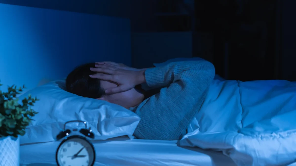 člověk v posteli s rukama na obličeji