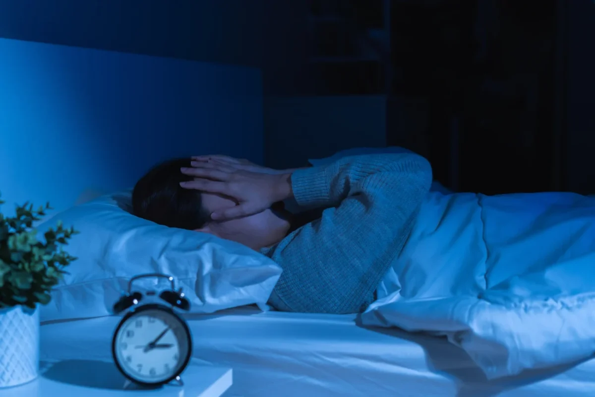 člověk v posteli s rukama na obličeji