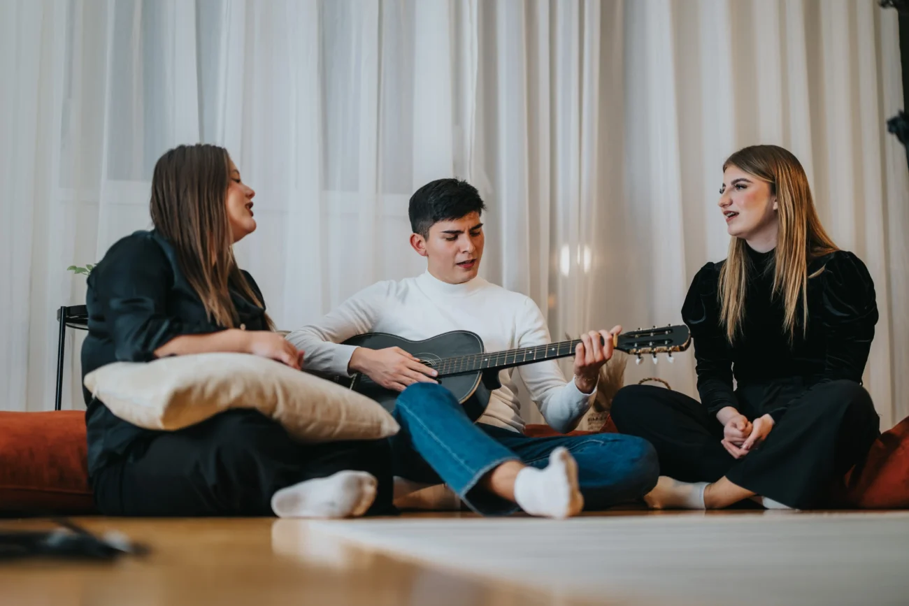 Tři lidé zpívající s kytarou na gauči. 