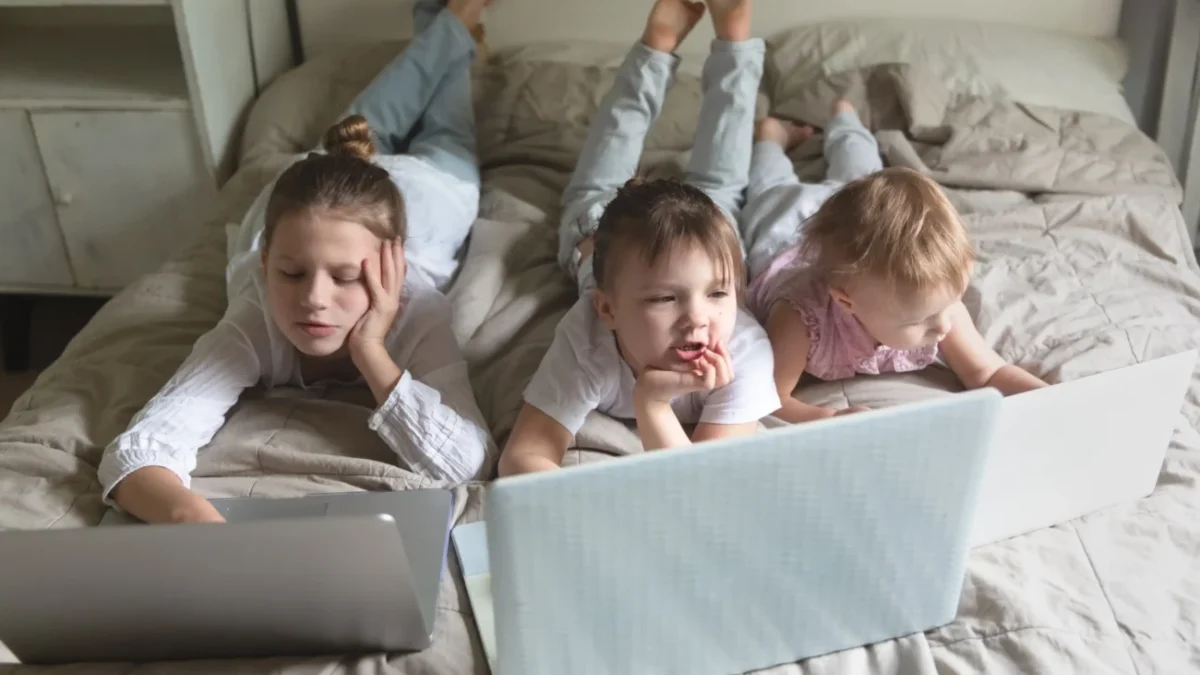 Děti leží na posteli u notebooků.
