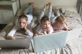 Děti leží na posteli u notebooků.