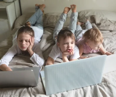 Děti leží na posteli u notebooků.