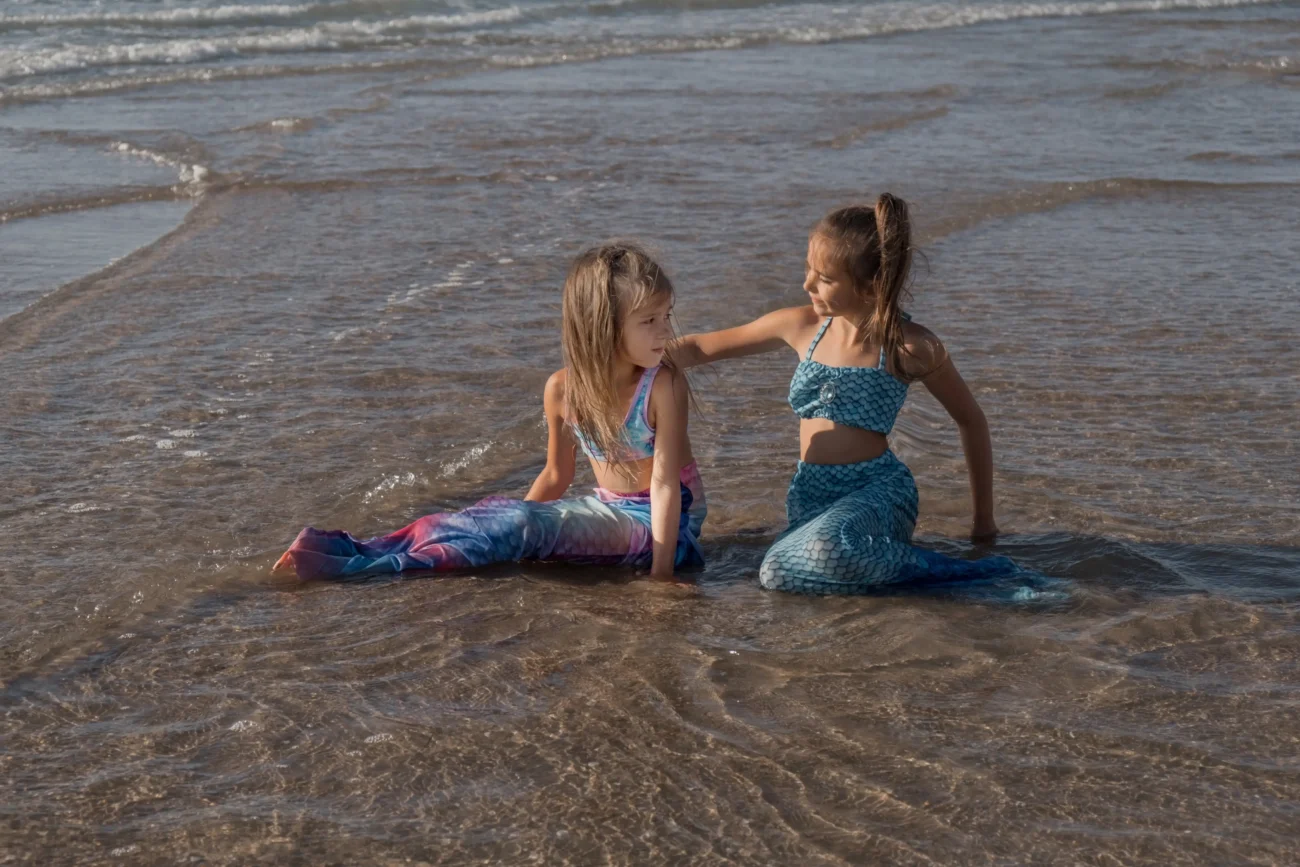 Děti si hrají na pláží jako mořské panny.