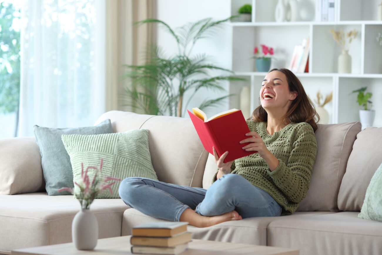 HappyWomanLaughingReadingAFunnyComedyBookSittingOn | TVGURU.cz smích