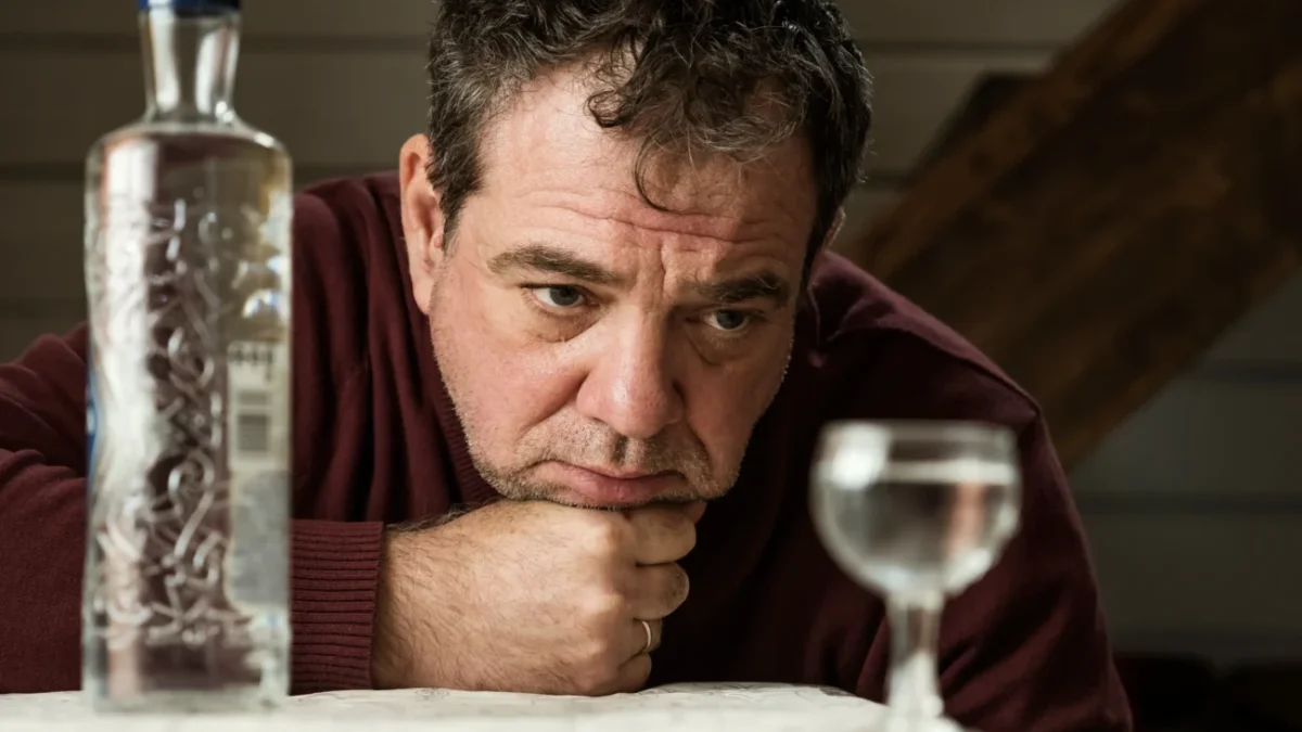 Muž se dívá na skleničku s alkoholem.