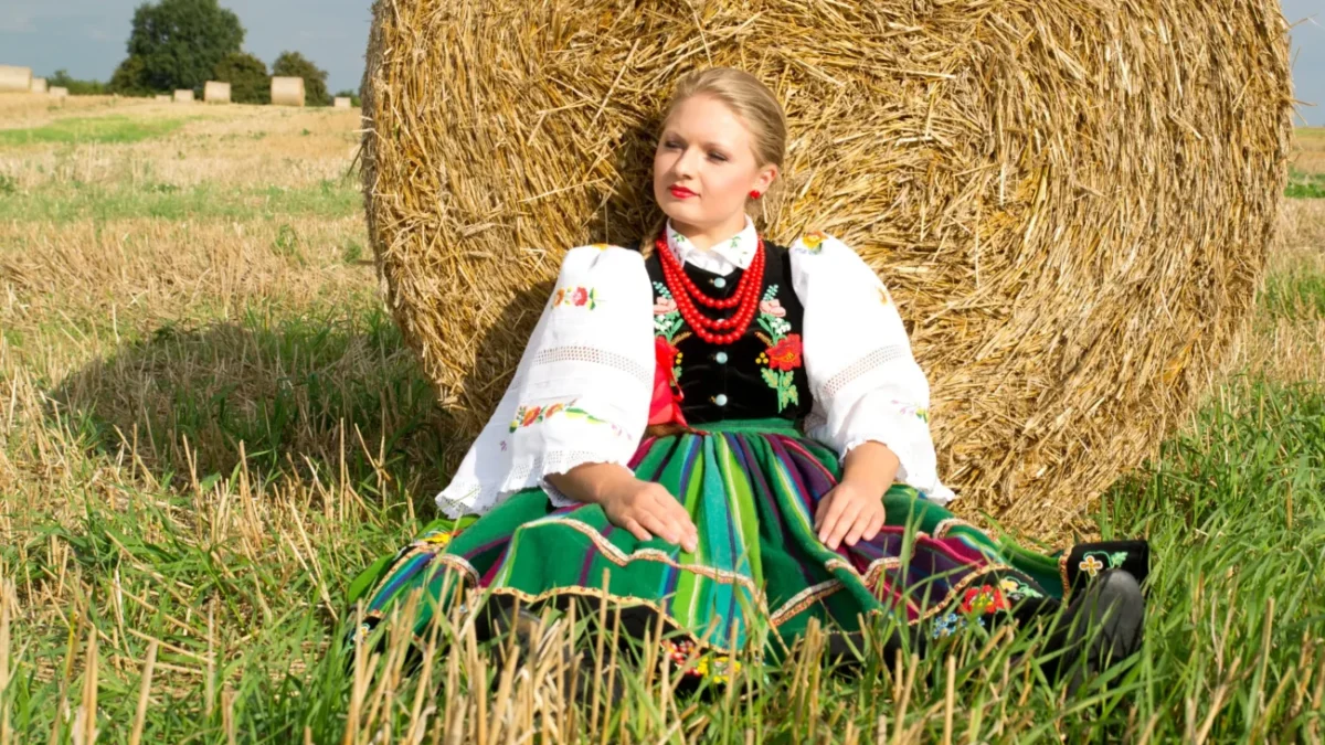 Žena v polském kroji sedí u balíku sena.