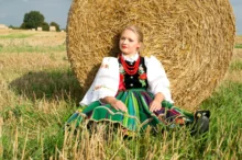 Žena v polském kroji sedí u balíku sena.