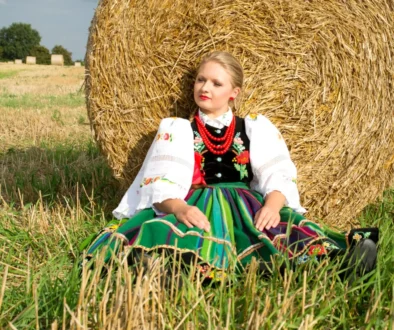 Žena v polském kroji sedí u balíku sena.