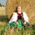 Žena v polském kroji sedí u balíku sena.