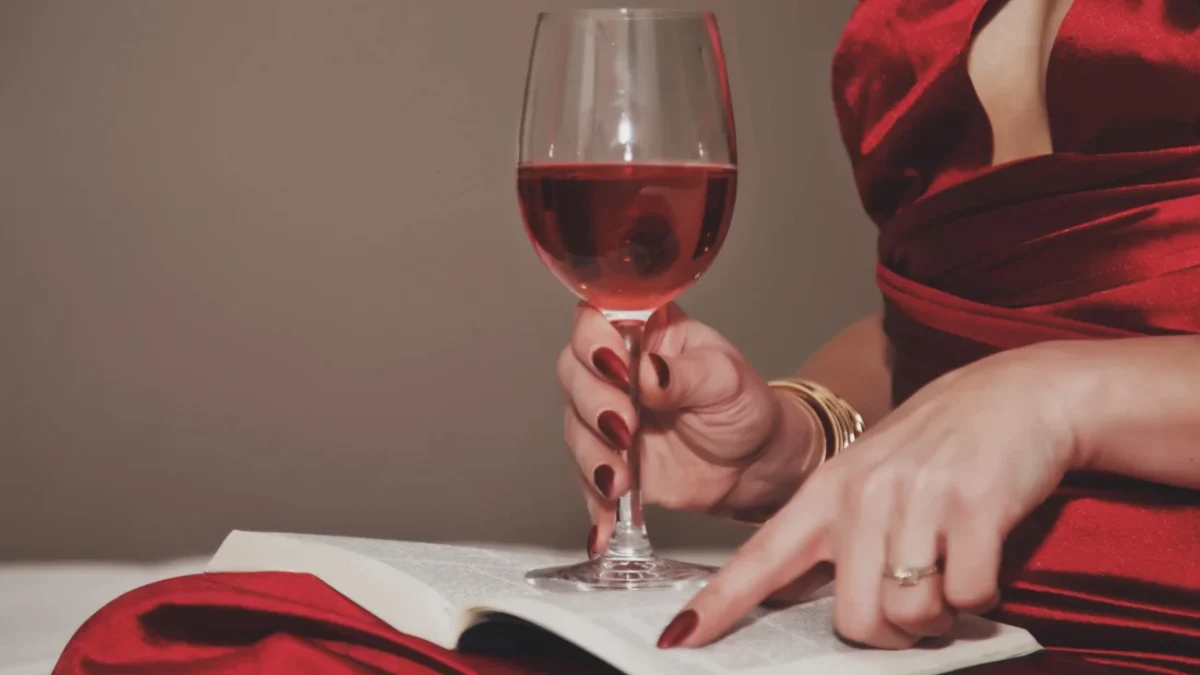 Žena v ruce drží knihu a sklenku s vínem.