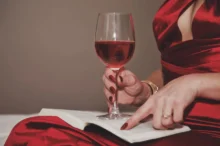 Žena v ruce drží knihu a sklenku s vínem.