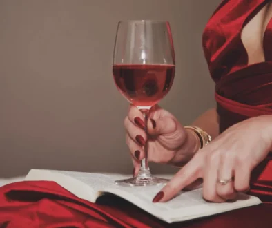 Žena v ruce drží knihu a sklenku s vínem.