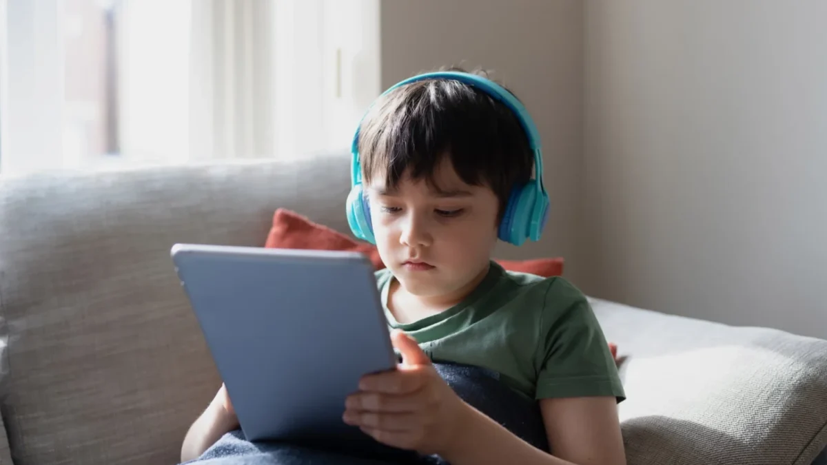 Chlapeček je na tabletu a na uších má sluchátka.