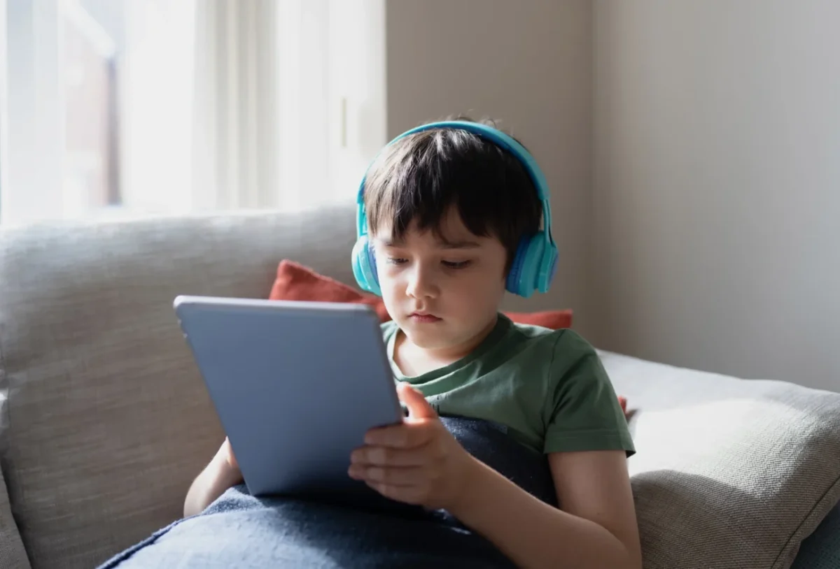 Chlapeček je na tabletu a na uších má sluchátka.
