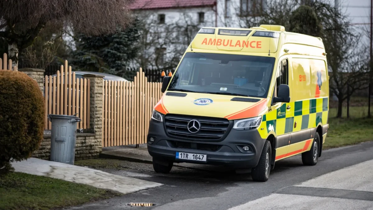 Před plotem stojí sanitka.