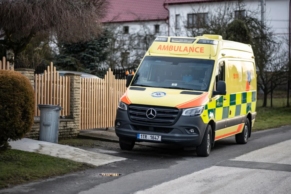 Před plotem stojí sanitka.