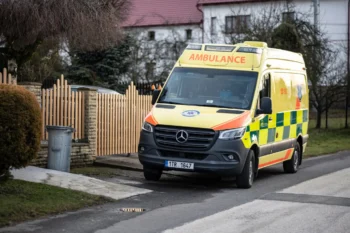 Před plotem stojí sanitka.