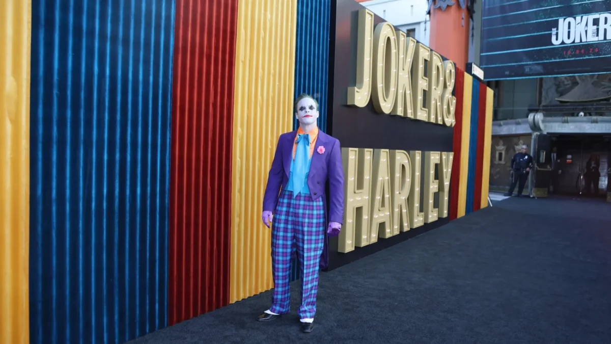Před nápisem Joker stojí muž za Jokera přestrojený.