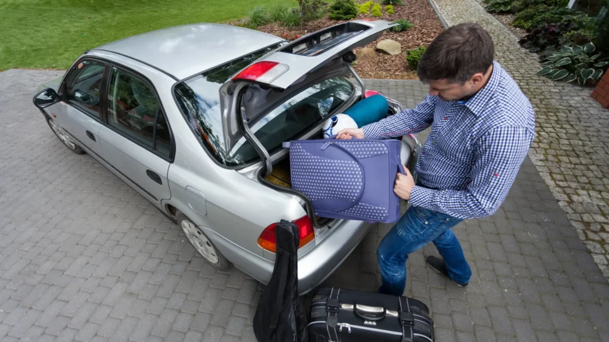 Muž nakládá kufry do auta.