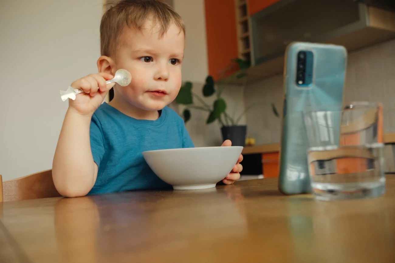 Chlapeček se u stolu dívá na něco na telefonu. 
