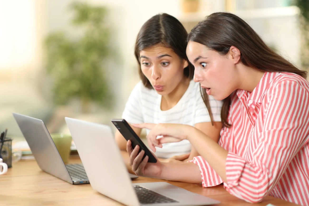 Dvě ženy koukají do telefonu a diví se. 