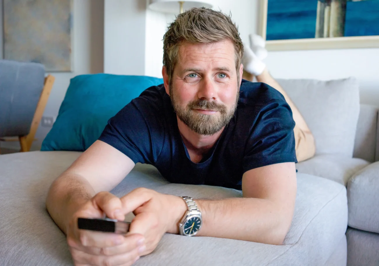 Muž s ovladačem v ruce leží na pohovce.