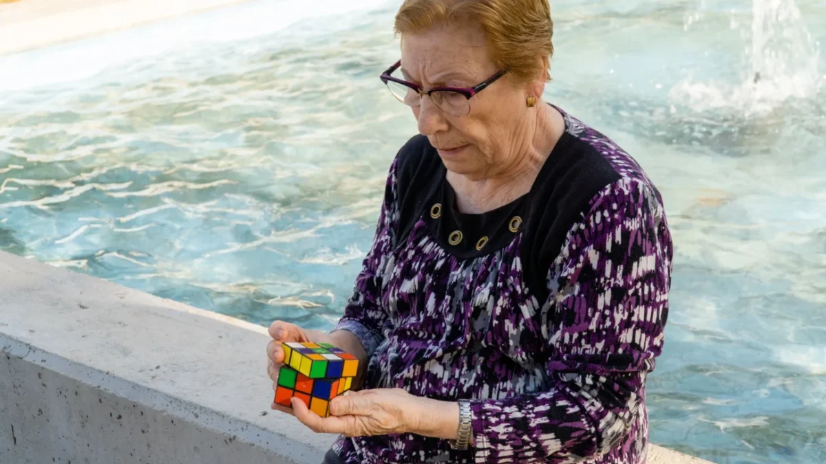 Babička sedí u fontány a skládá Rubikovu kostku.