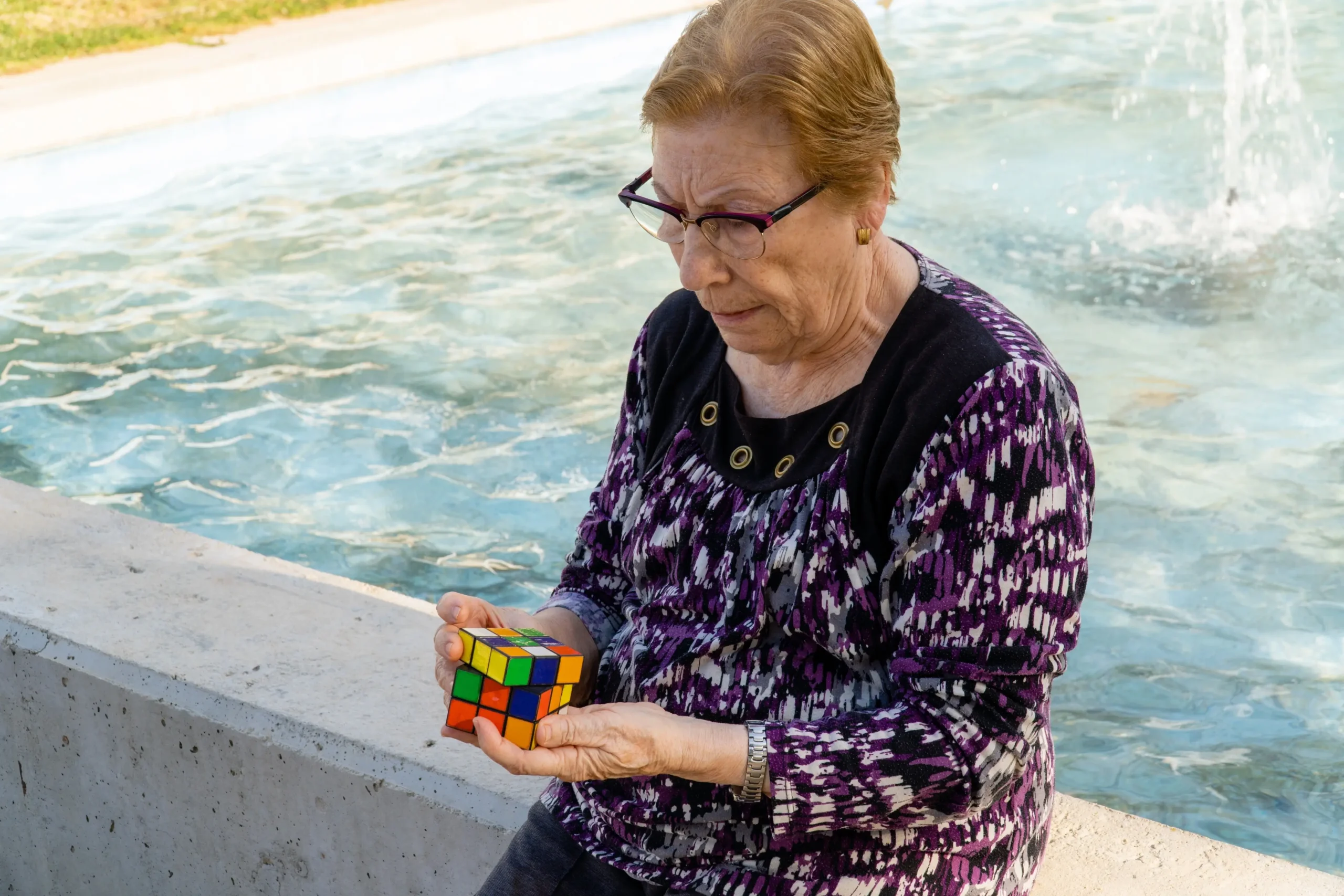 Babička sedí u fontány a skládá Rubikovu kostku.