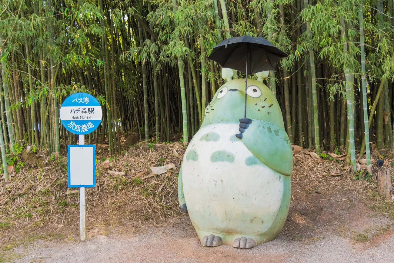 Totoro stojí s deštníkem u zastávky. 