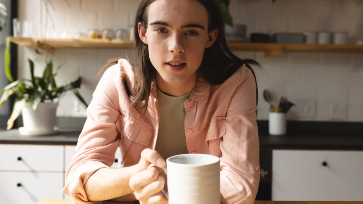 Trans muž sedí u stolu s hrnkem v ruce.